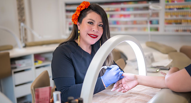 a woman smiling while doing nails at a customer
